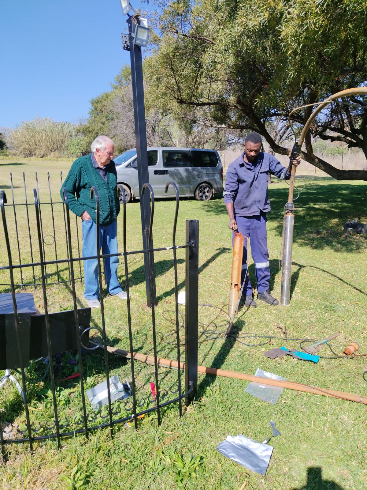 BoreFixPro technician handling a submersible pump on a client's property while the estate owner observes